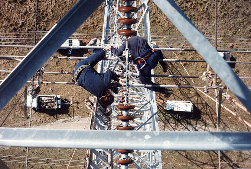 Riggers installing insulator chains on top of a tower.